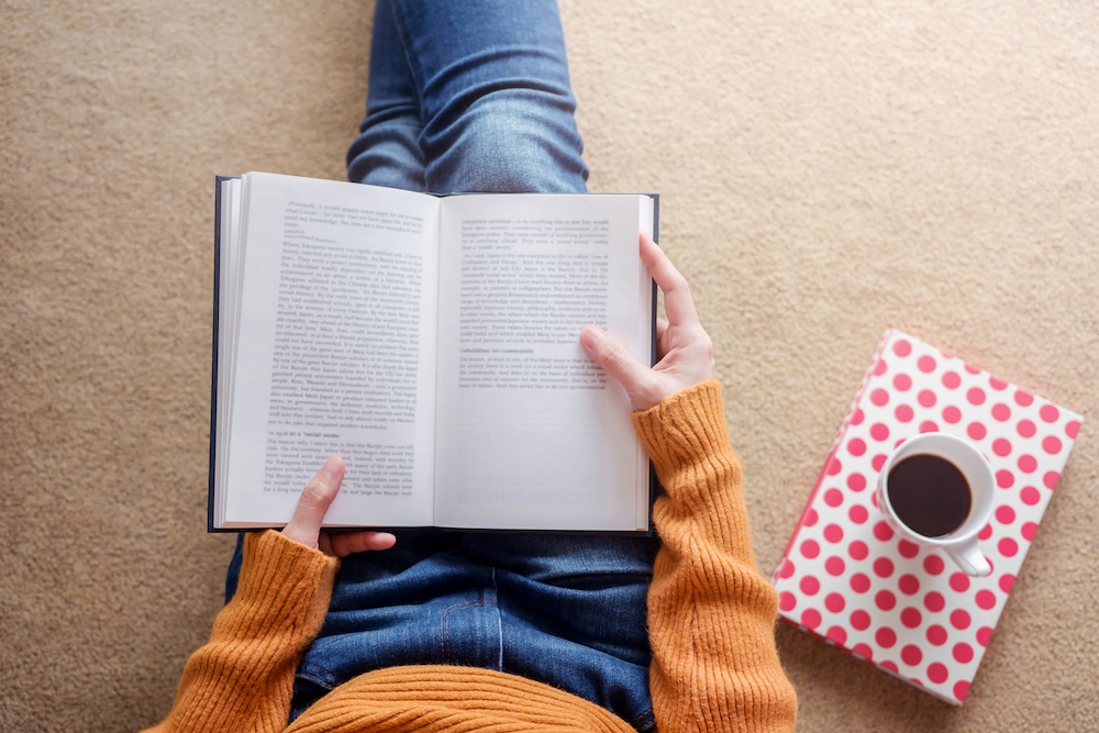 Reading Concept. Soft Focus of Young Woman Relaxing by Book and Coffee in Cozy House, Sit on the Floor, Top View